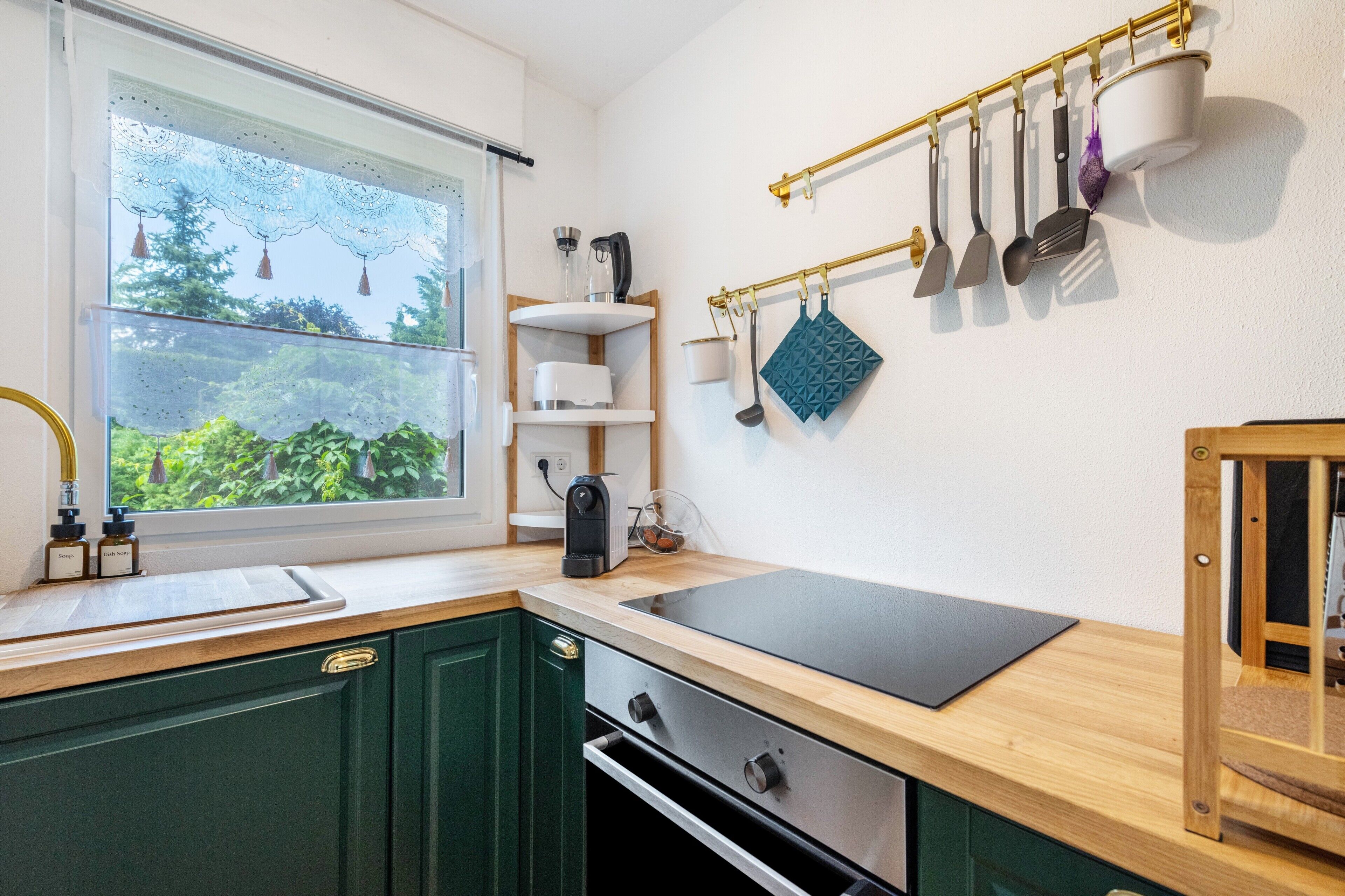 Eine Küche mit Fenster, Holdekor, einer schwarzen Arbeitsplatte und einer an der Decke befestigten Küchenutensilienstange.
