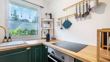 Eine Küche mit Fenster, Holdekor, einer schwarzen Arbeitsplatte und einer an der Decke befestigten Küchenutensilienstange.