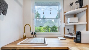 Une cuisine avec un plan de travail en bois, un évier, une fenêtre donnant sur un espace verdoyant et une machine à café.