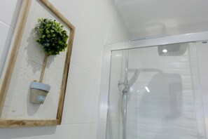 A framed plant with a tag, a glass shower enclosure, and a white tiled wall.