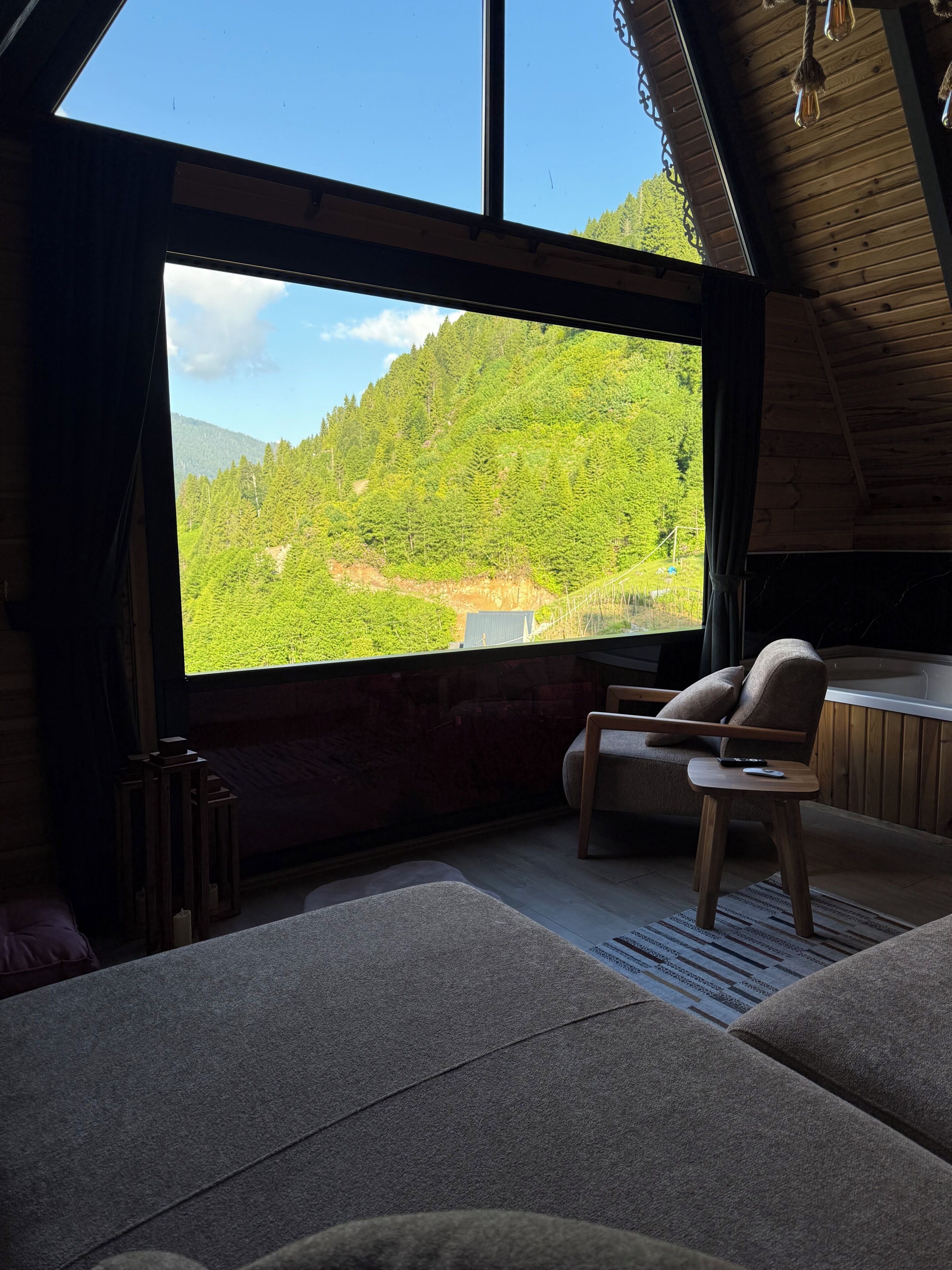 Ein gemütliches Zimmer mit großem Fenster, Holzbalkendecke und einer Sitzecke mit Sessel und kleinem Tisch.