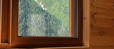 A wooden cabin with a dining table set for breakfast, a window with a mountain view, and a wooden interior.