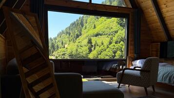 Un dormitorio tipo loft con un ventanal grande, una escalera de madera, un sofá, una silla y una cama.
