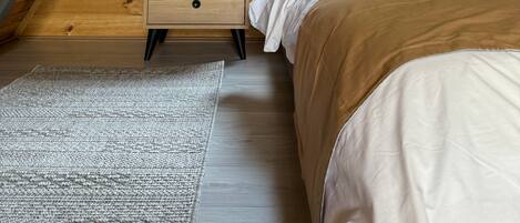Une chambre avec un plafond en pente, une fenêtre avec des rideaux, un lit, une table de chevet et un tapis.