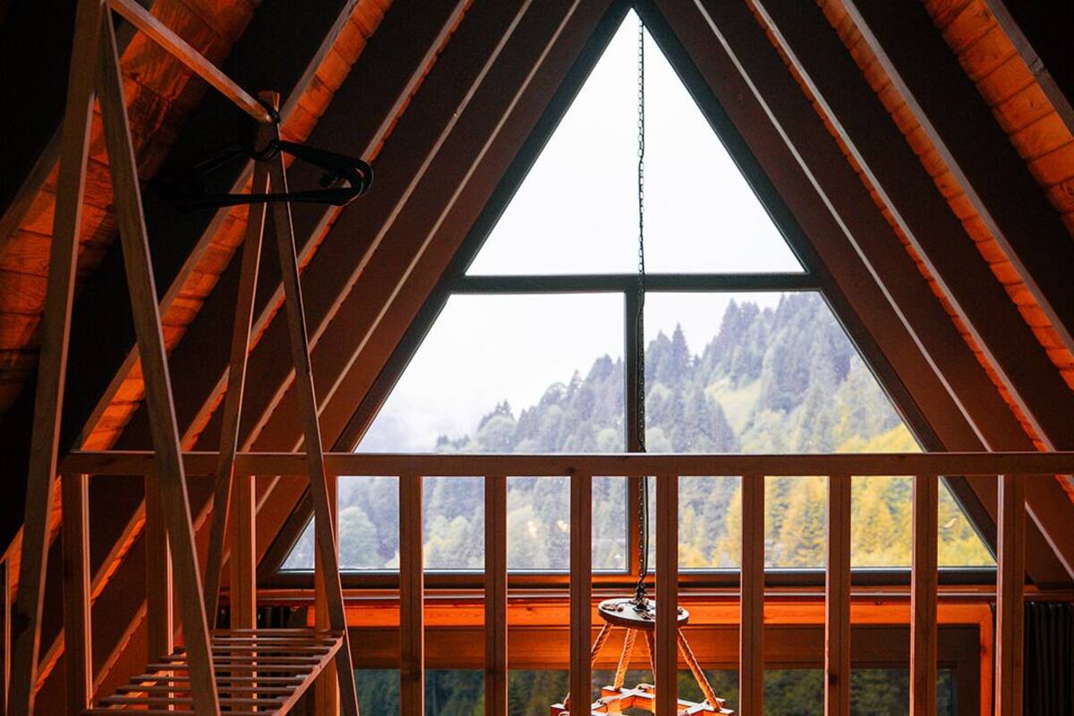 Et rum med højt til loftet og et stort vindue der udover et bjerglandskab, en træstige og en hængende lampe.