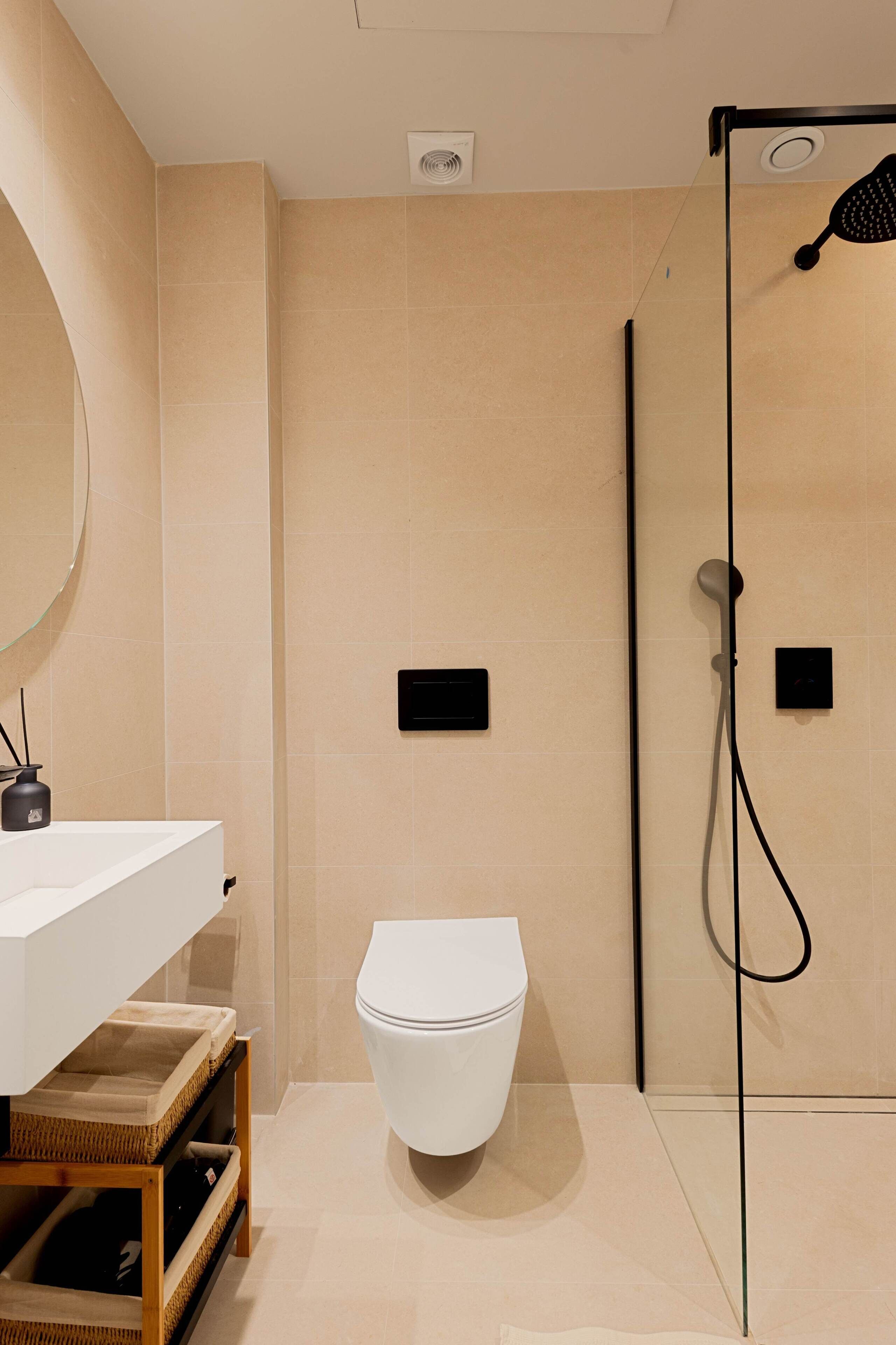 A modern bathroom with a white toilet, a glass shower enclosure, and a white sink with a mirror.
