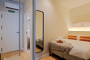 Ett hotellrum med en säng, en spegel, en garderob och en väggmonterad luftkonditioneringsanläggning.