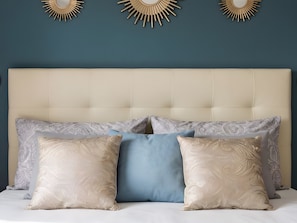 Ein Bett mit einem gebürsteten Kopfteil, drei an der Wand befestigte Sonnenstrahlspiegel und vier Kissen mit Muster.
