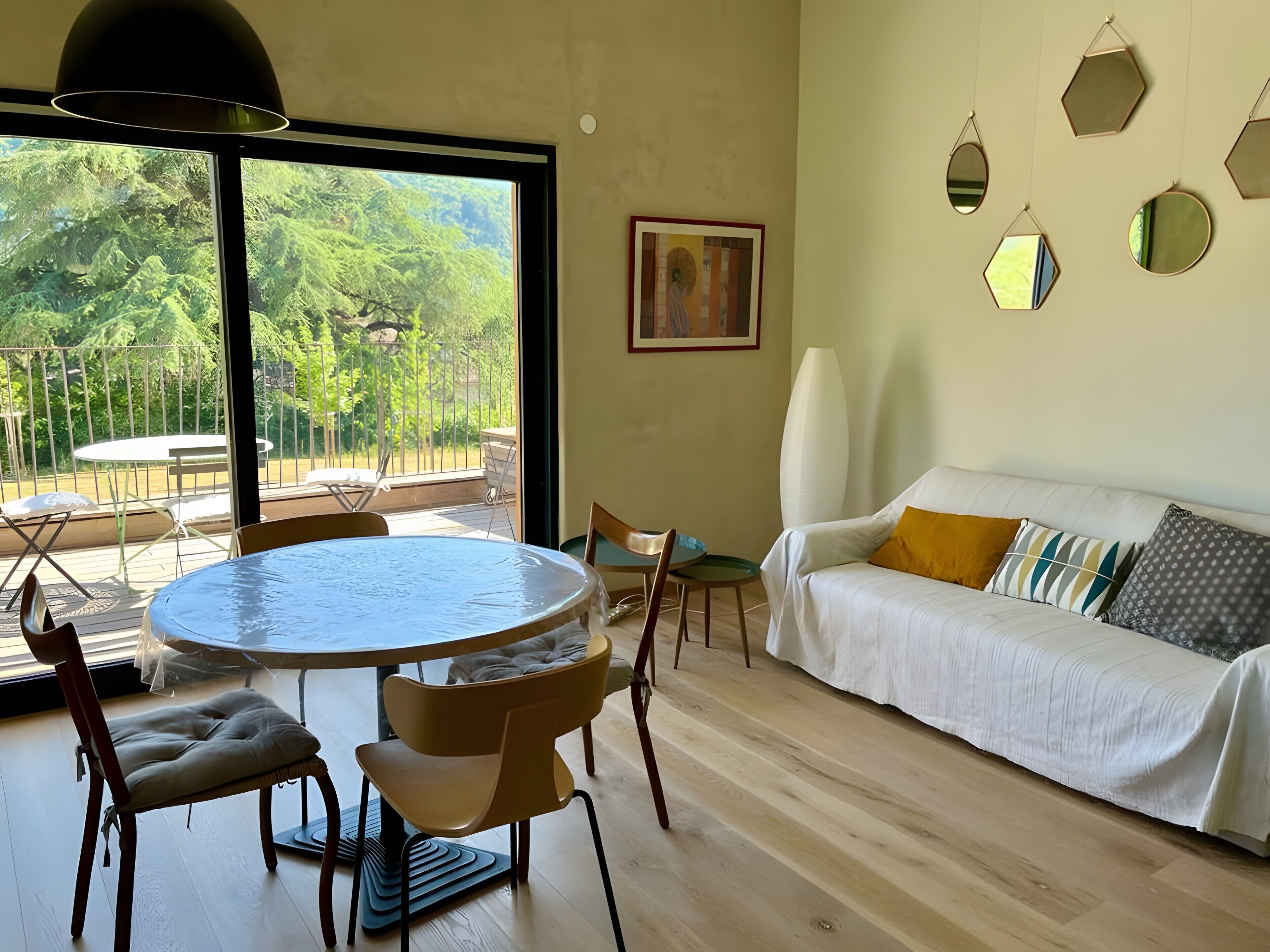 Un salon moderne avec une table à manger ronde, un canapé agrémenté de coussins et une grande fenêtre donnant sur un paysage verdoyant.
