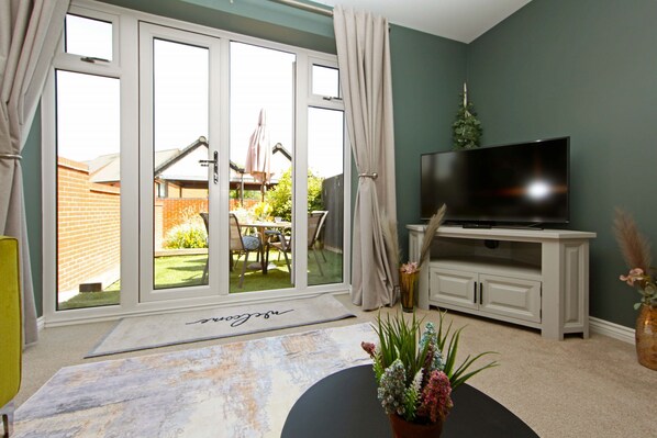 A living room with a television on a white cabinet, a sliding glass door leading to a patio, and a rug with a name on it.