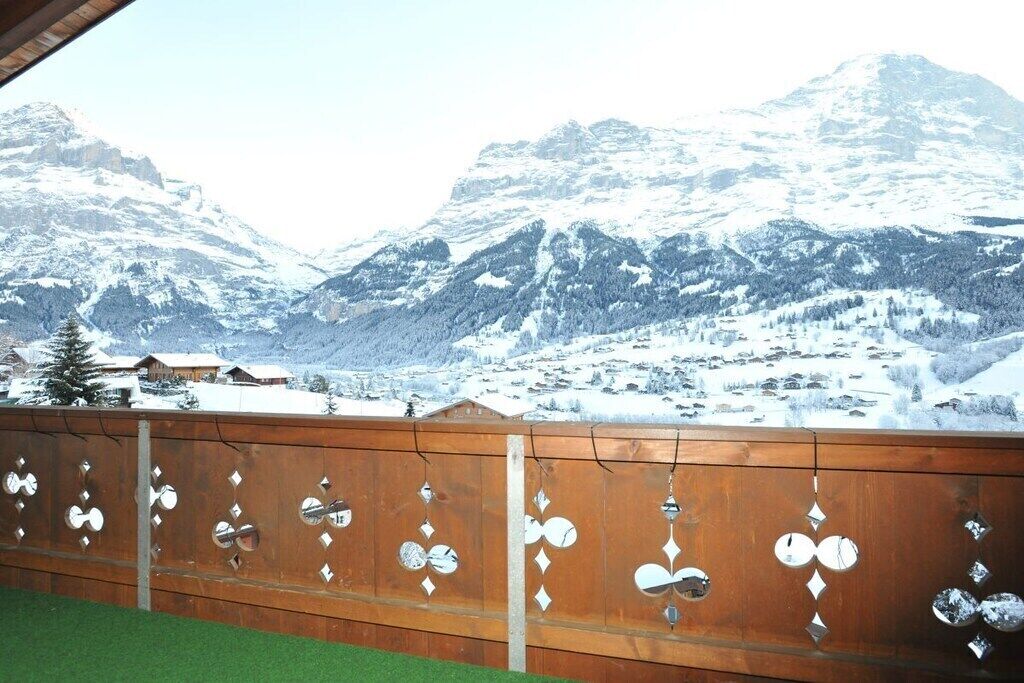 Un balcon en bois, agrémenté de décorations en métal, qui offre une vue sur un paysage montagneux enneigé.