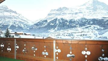 Un balcon en bois, agrémenté de décorations en métal, qui offre une vue sur un paysage montagneux enneigé.