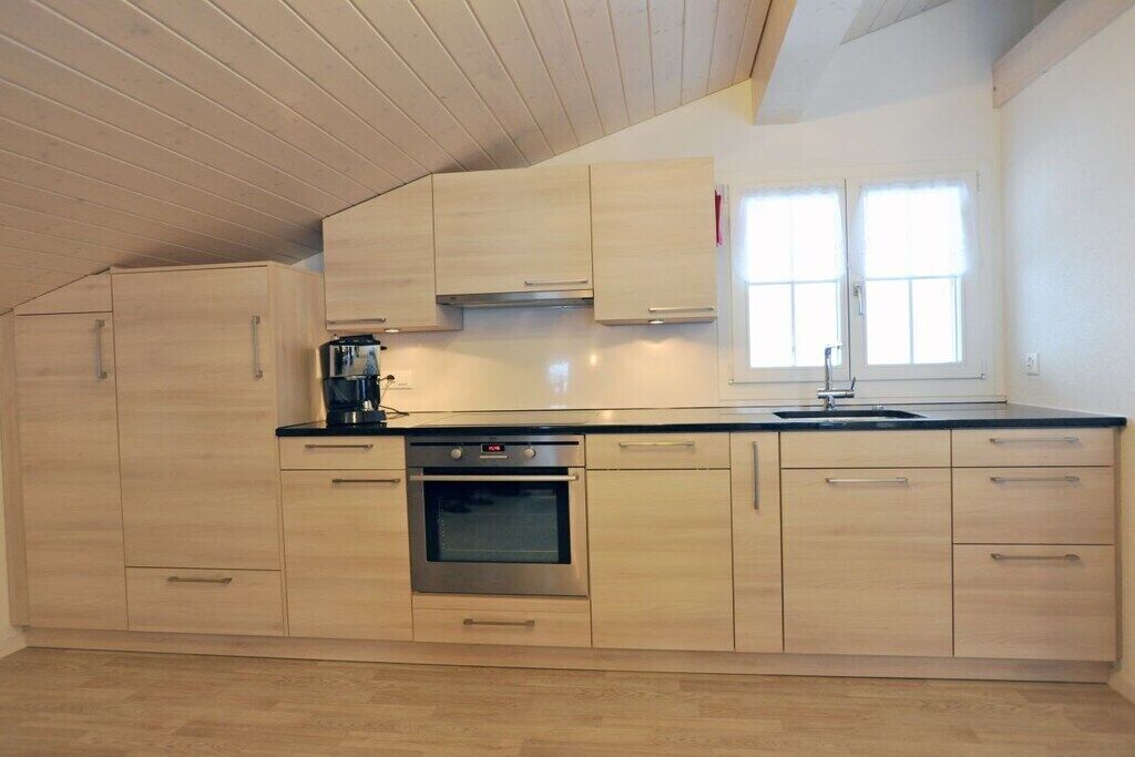 Une cuisine moderne avec des meubles en bois, un four en acier inoxydable et une fenêtre équipée de stores.