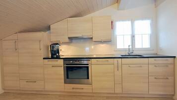 Une cuisine moderne avec des meubles en bois, un four en acier inoxydable et une fenêtre équipée de stores.