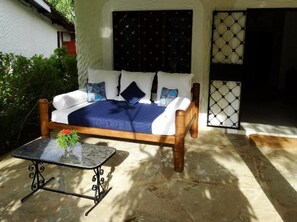 A bed with white and blue bedding, a small table with a vase, and a window with a patterned curtain.