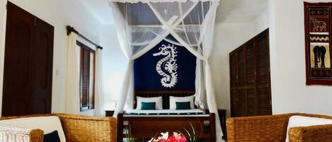 Una habitación con dos sofás de mimbre, una cama con dosel y una pared con un emblema decorativo.