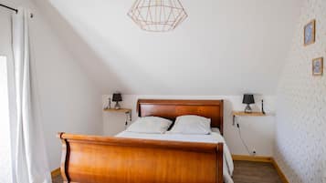 Een slaapkamer met een houten bed, twee nachtkastjes met lampen, een geometrisch hanglamp en een behang met patroon.