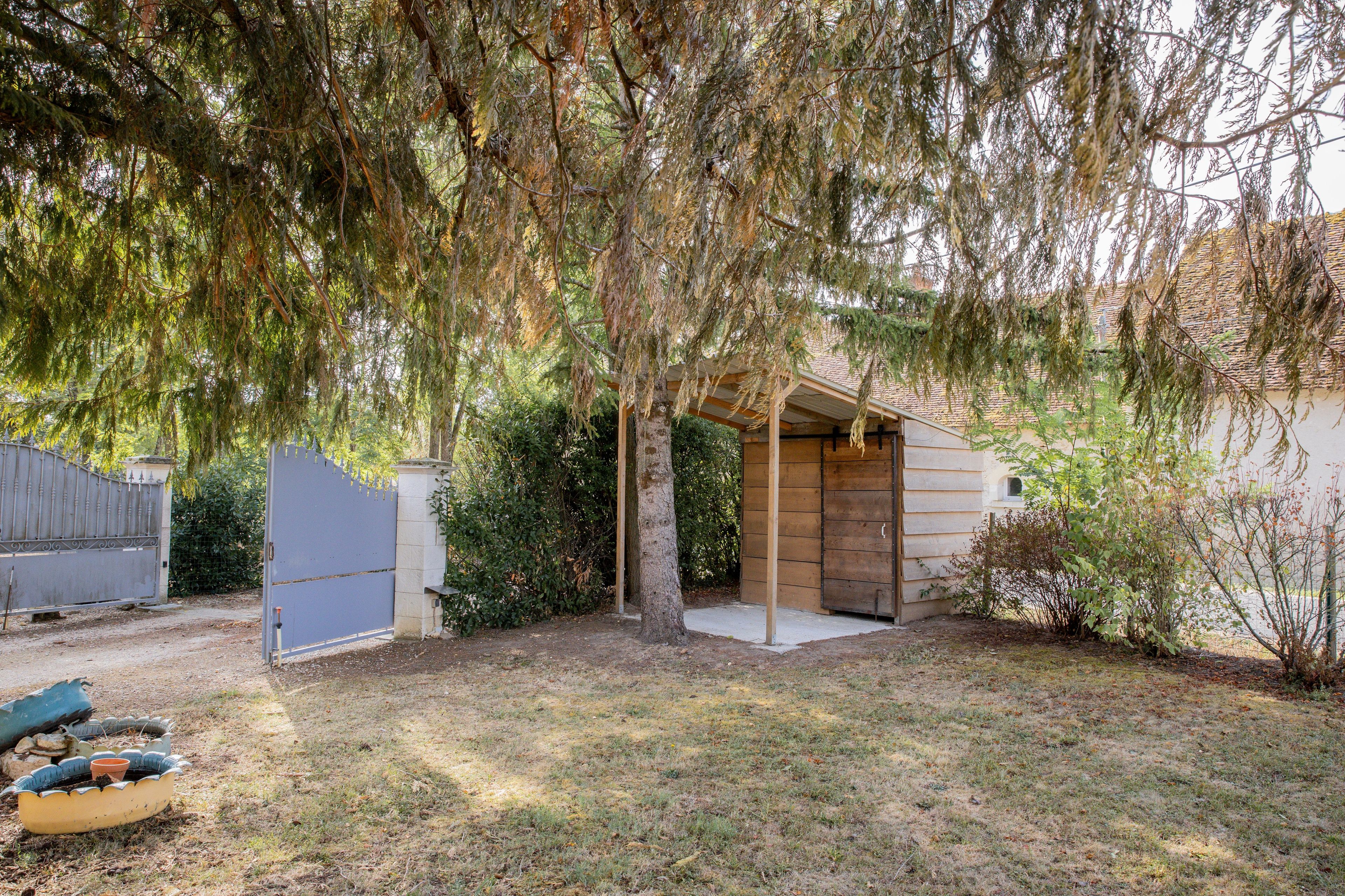 Un espace extérieur abrité, doté d’une structure en bois, d’un portail en métal et d’un petit jardin agrémenté d’un jardinière.