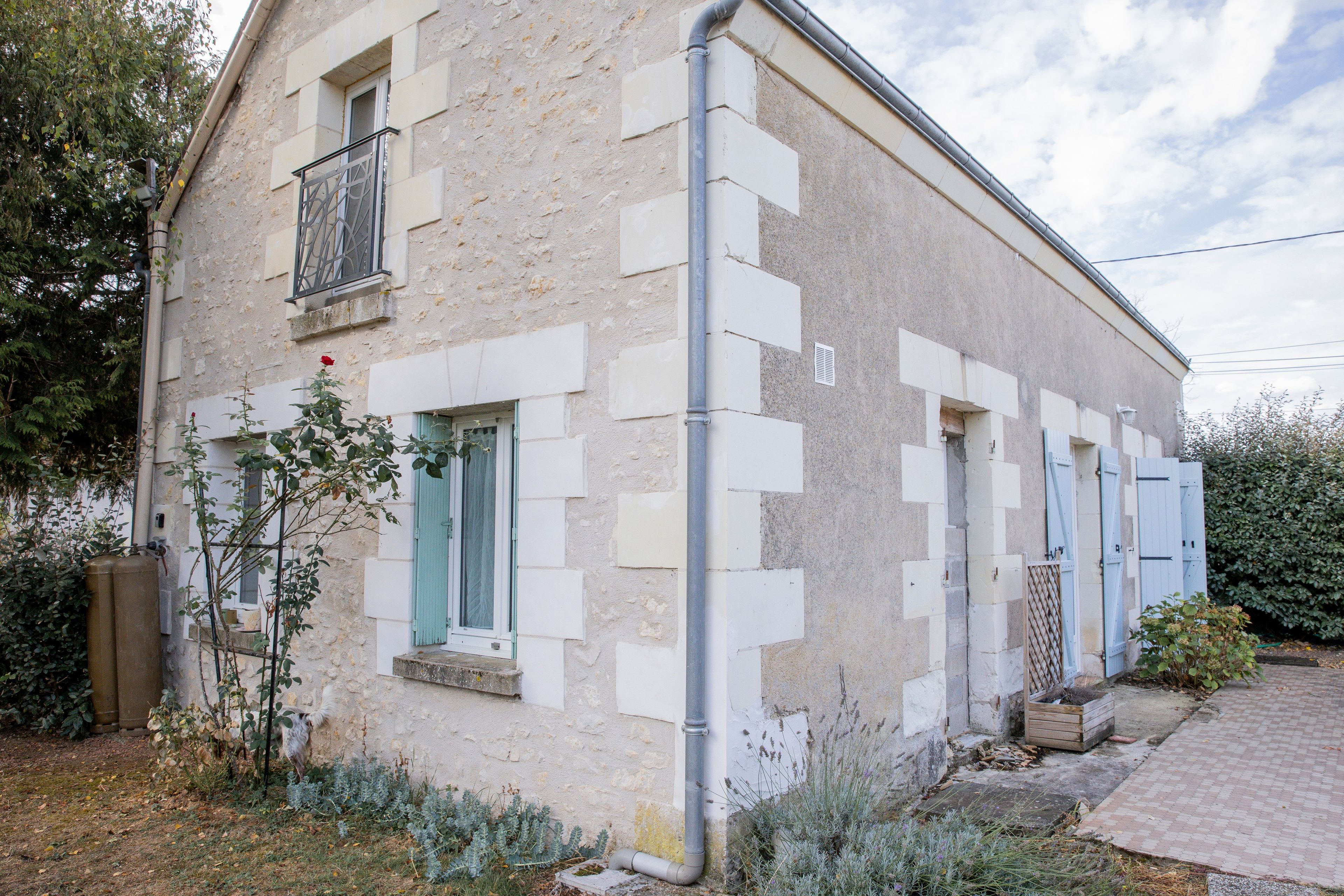 Um edifício de dois andares com fachada de pedra, várias janelas com persianas e um sistema de calhas visível.