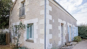 Um edifício de dois andares com fachada de pedra, várias janelas com persianas e um sistema de calhas visível.