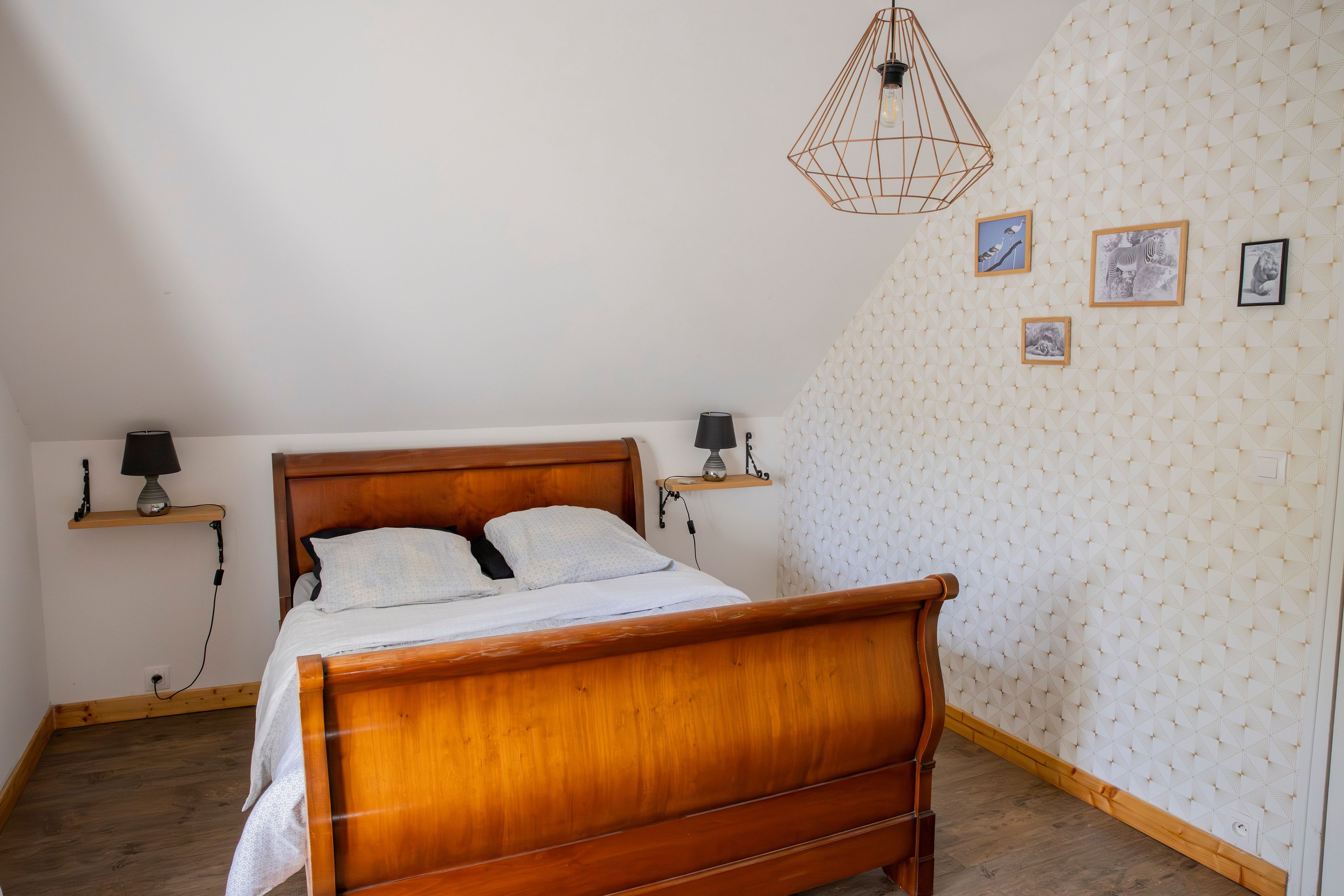 Une chambre à coucher avec un lit en bois, deux tables de chevet avec des lampes, un mur orné d’un motif géométrique et des tableaux encadrés.