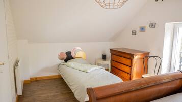 A bedroom with a bed, a wooden dresser, a bedside table with a lamp, and a hanging light fixture.