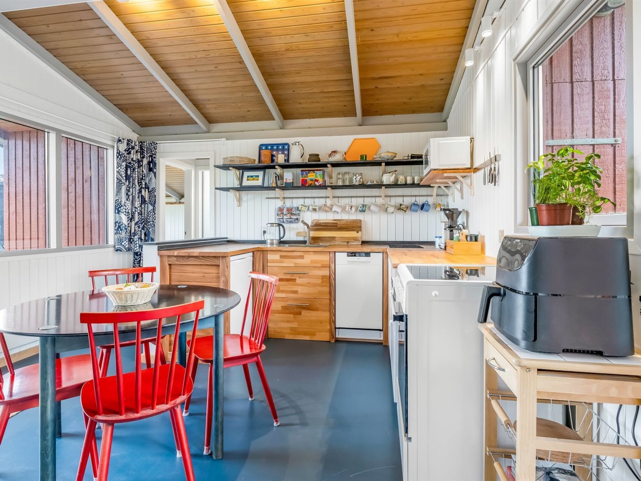 Eine Küche mit Holzboden, einem Esstisch mit roten Stühlen, einer Kaffeemaschine und einem Blumentopf am Fenster.
