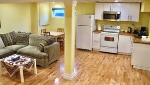 Una sala de estar con sofá, una mesa de centro y una zona de comedor con mesa y sillas. La cocina incluye un microondas, horno y refrigerador.