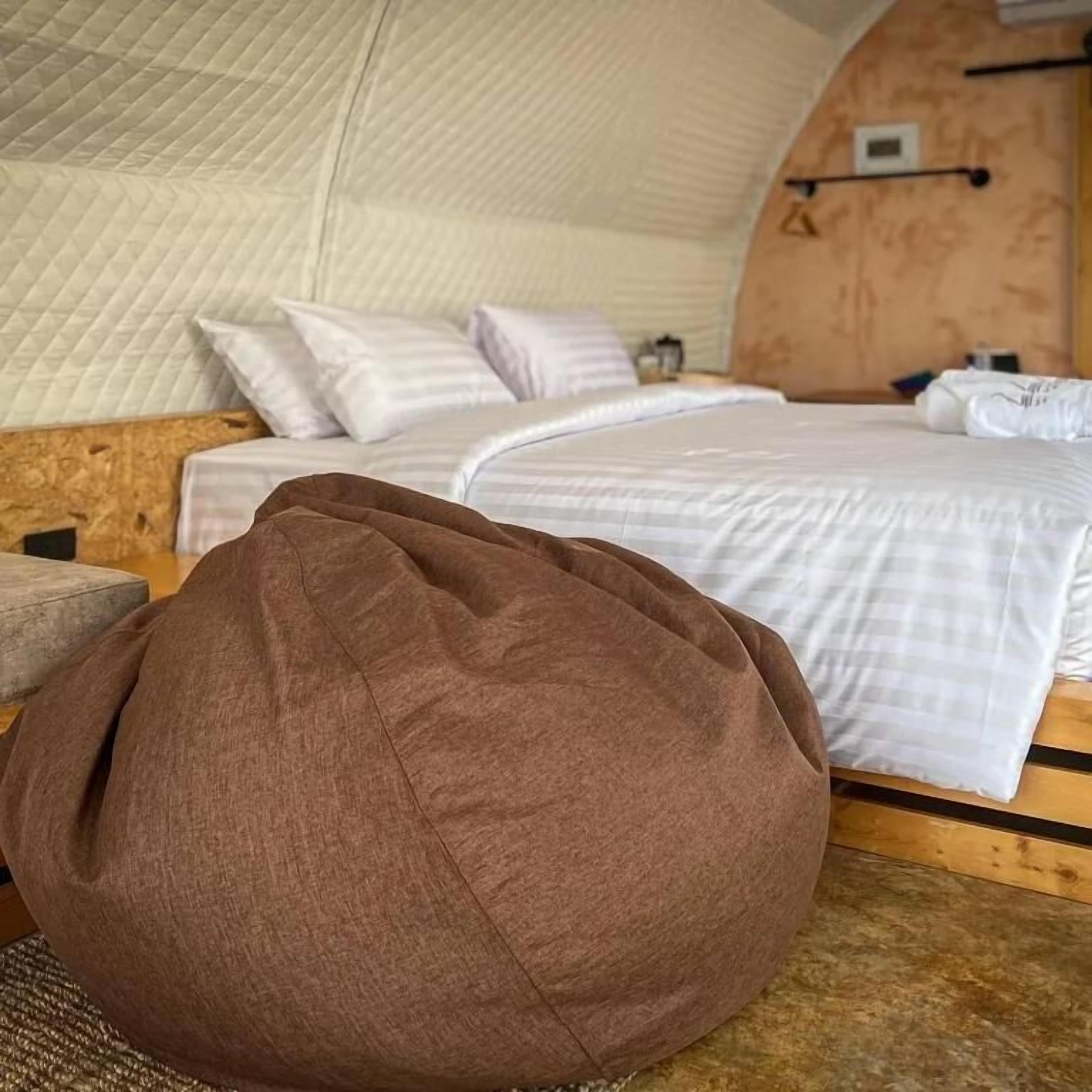 A cozy room with a bed, pillows, a wooden headboard, and a brown bean bag chair.
