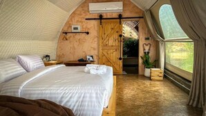A cozy, rustic tent-style bedroom with a bed, bedside table, and a large window.