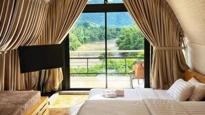 A bedroom with a large bed, a TV, and a view of greenery through a window.