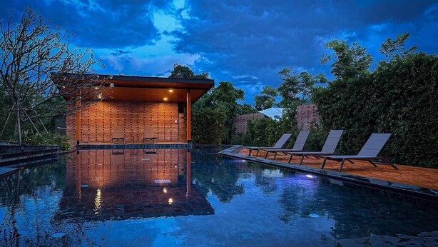 A swimming pool with lounge chairs, a brick building, and trees.