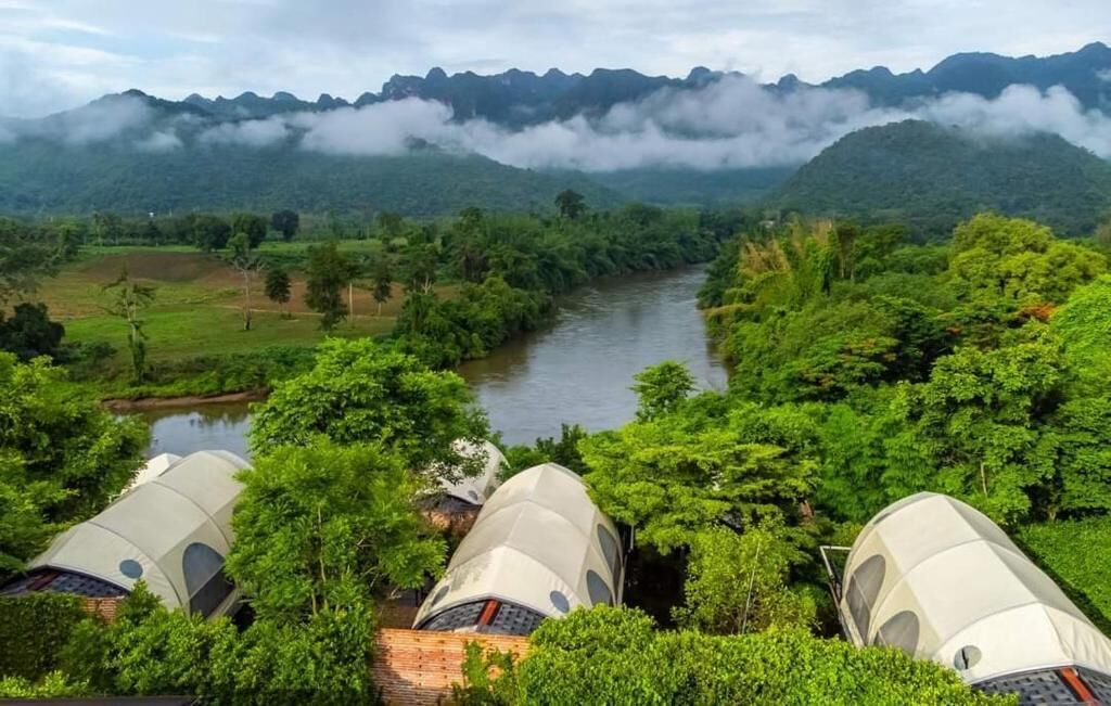 Un río rodeado de vegetación exuberante y montañas, con varias tiendas en forma de cúpula a la vista.