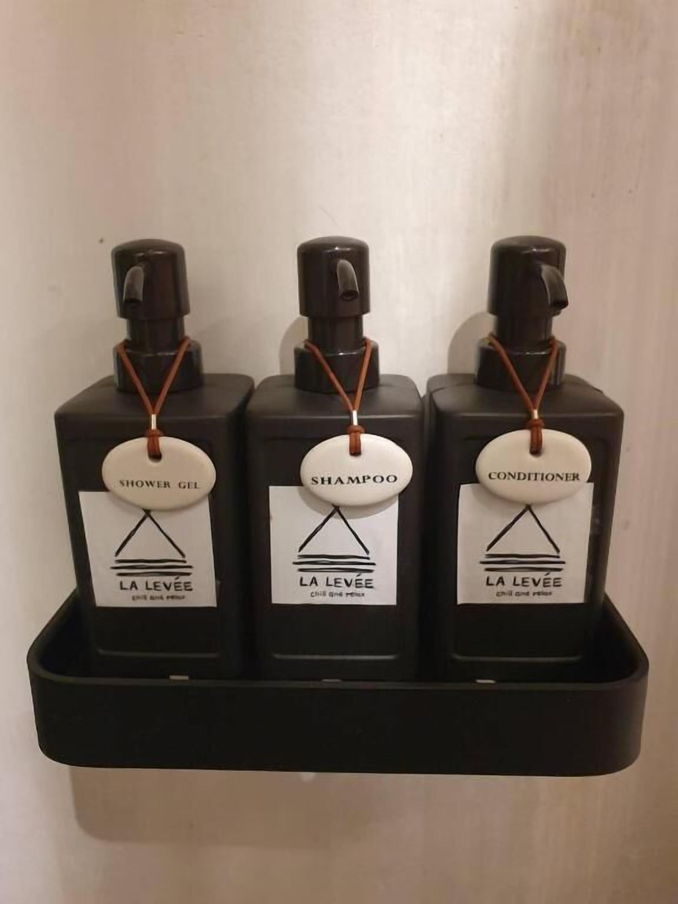Three bottles of La Levee products: shower gel, shampoo, and conditioner, each with a black pump dispenser and a white label with a black triangle logo.