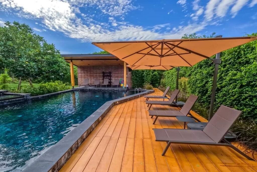 Een houten terras met een zwembad, ligstoelen en een bakstenen gebouw.