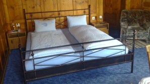 A wooden-paneled room with a metal-framed bed, two bedside tables, and a chair. - Ferienwohnungen Chasa Valär, (Scuol) by Interhome (Scuol)