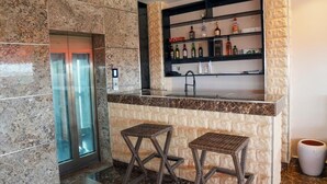 A bar area with a marble counter, two wicker stools, and a shelf with bottles. - Waveline Apartment (Abuja)