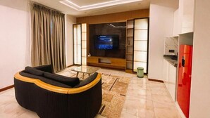 A modern living room with a sofa, a flat-screen TV, and a kitchen area with a refrigerator. - Waveline Apartment (Abuja)