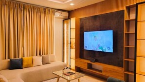 A modern living room with a large flat-screen TV, a sofa, a coffee table, and a bookshelf. - Waveline Apartment (Abuja)