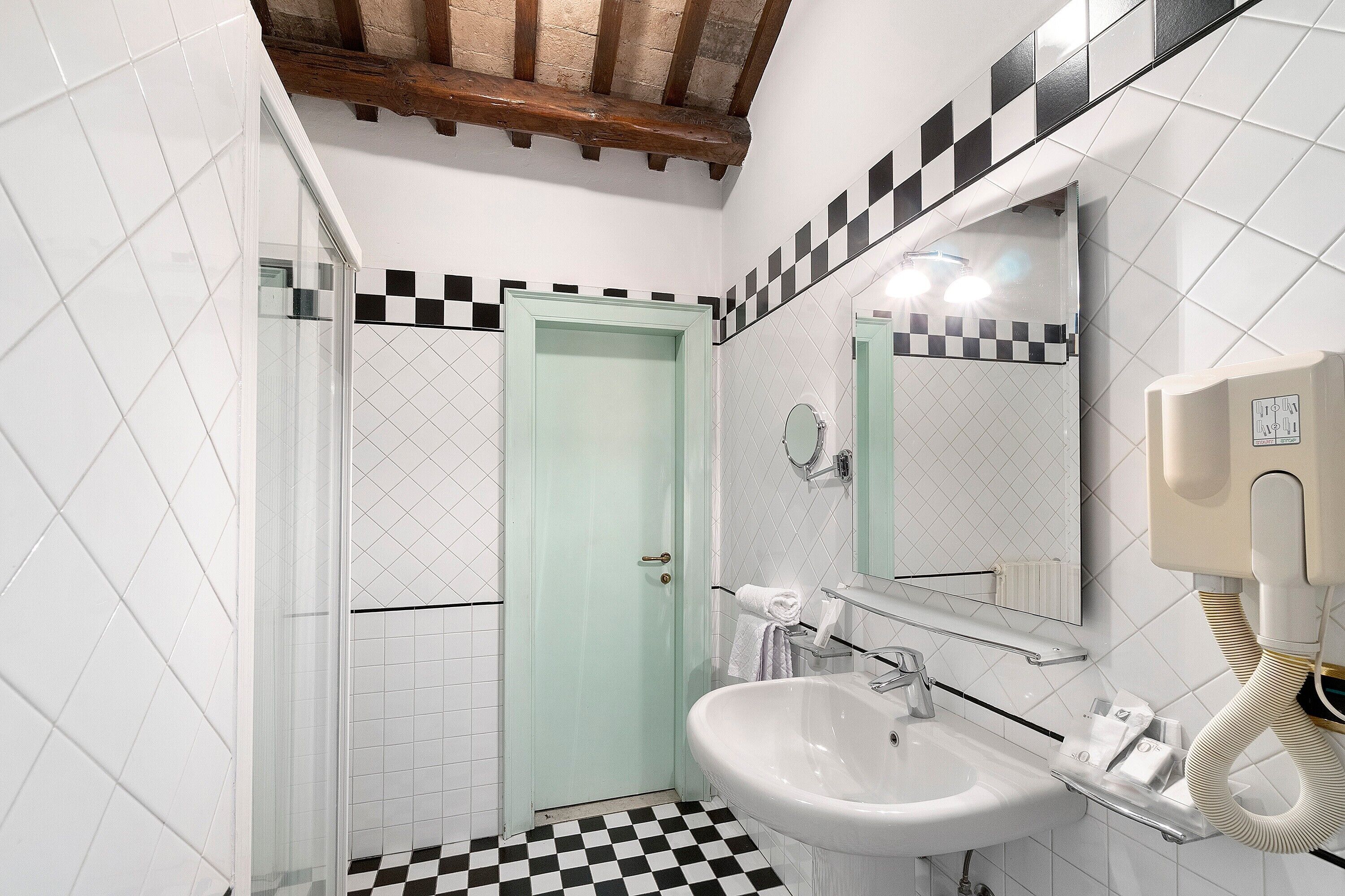 Een badkamer met een geruite vloer, een wastafel, een spiegel en een douche.