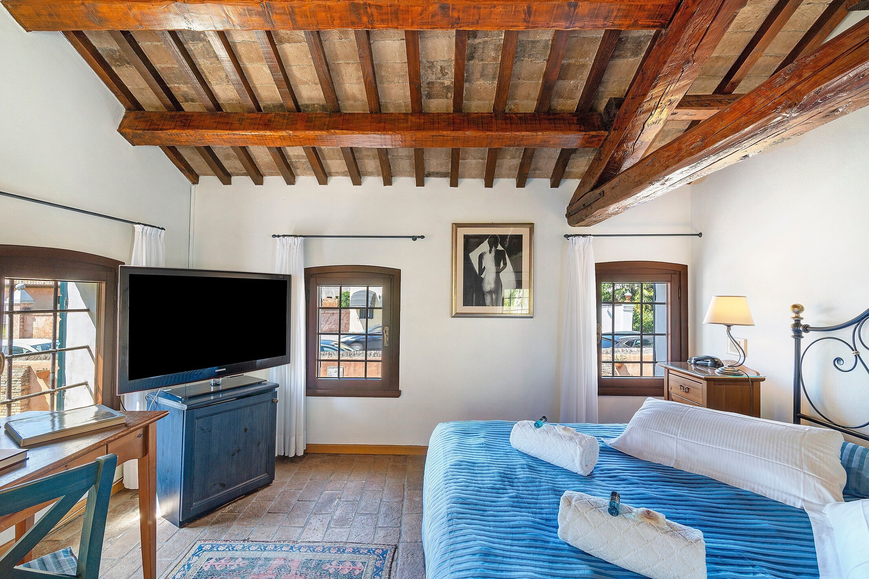 A bedroom with a bed, a television, a desk, and a window.
