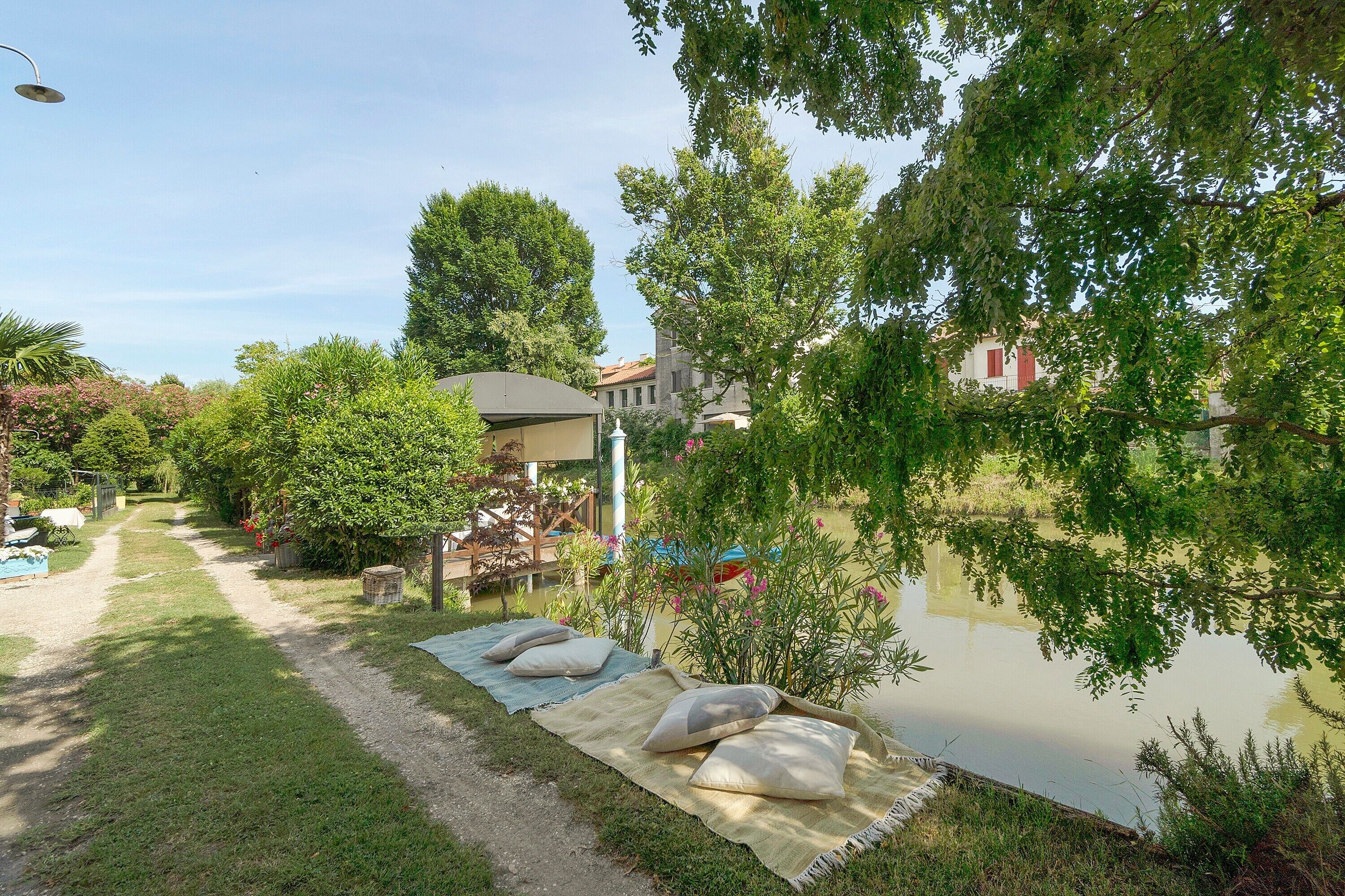 Um jardim com lago, um caminho e uma área de estar coberta com almofadas.