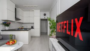Une cuisine moderne avec des meubles blancs, un coin repas doté d’une table blanche et un grand logo Netflix sur le mur.