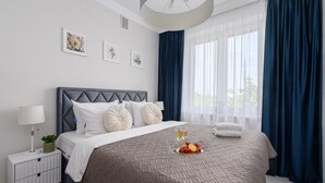 Une chambre à coucher moderne avec une couvre-lit à motifs géométriques, une tête de lit capitonnée et une table de chevet agrémentée d’une lampe et d’une plante.