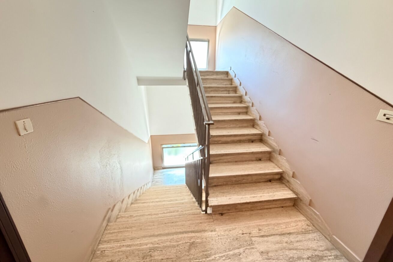 Een trap met een leuning, bekleed met tapijt, en een lichtschakelaar aan de muur.