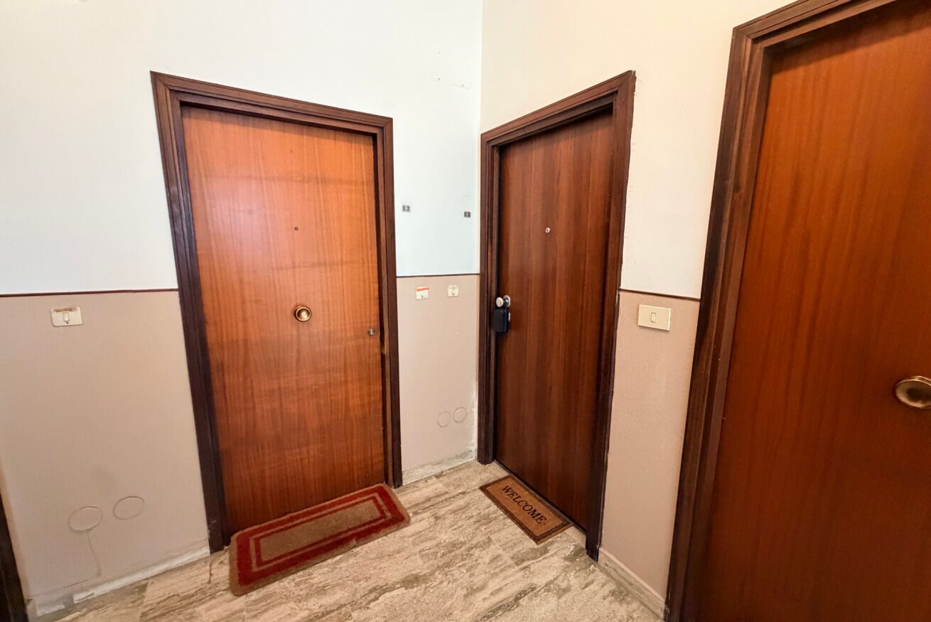 Un corridoio con tre porte in legno, un tappetino d'ingresso e un interruttore a muro.
