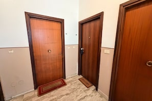 A hallway with three wooden doors, a welcome mat, and a light switch on the wall.