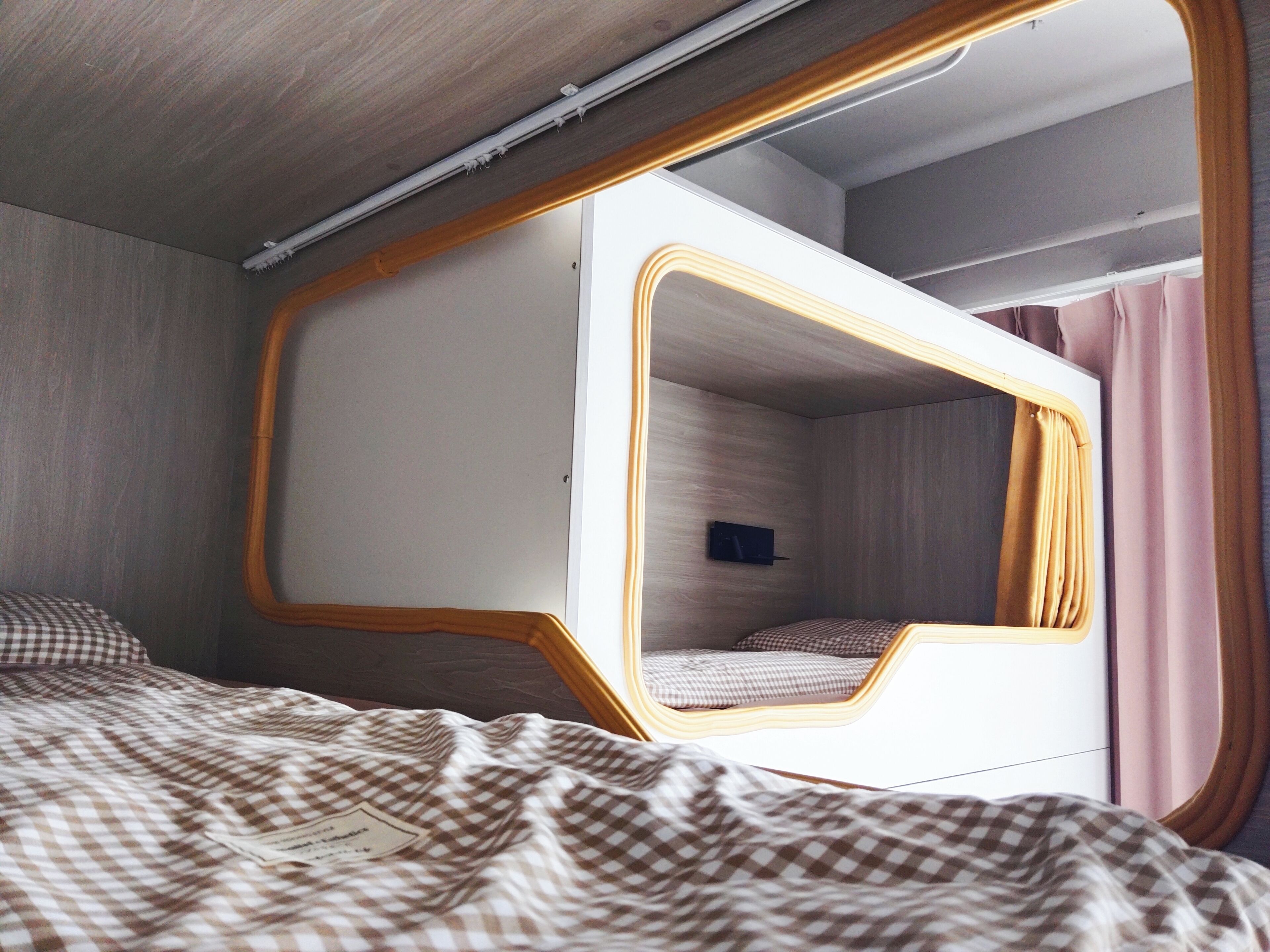 Una cama litera con estructura de madera, un espejo, una colcha de cuadros y un televisor fijado a la pared.