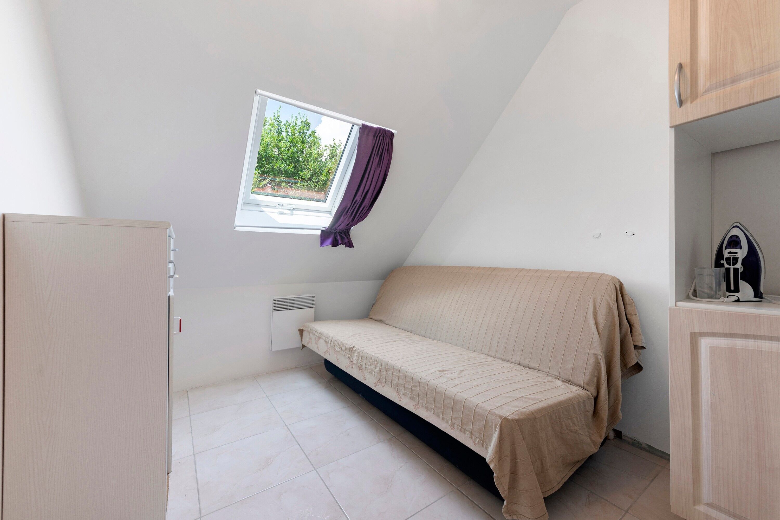 Eine kleine Einzimmerwohnung mit Bett, einem Vorhangfenster, einer Heizung und einer Küchenzeile.