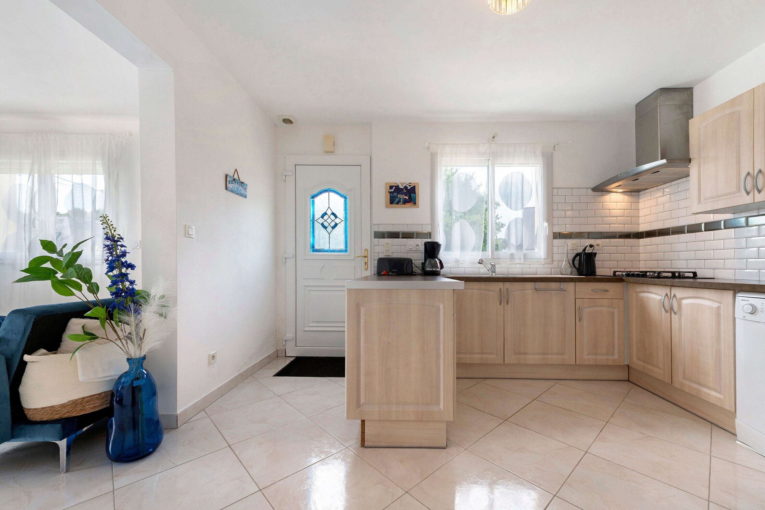 A modern kitchen with a central island, light wood cabinets, and a white tiled backsplash.